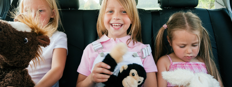 three happy young girls in the car with teddy bears