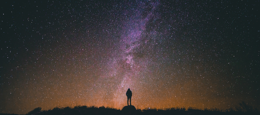 Person standing under a dark night sky stargazing