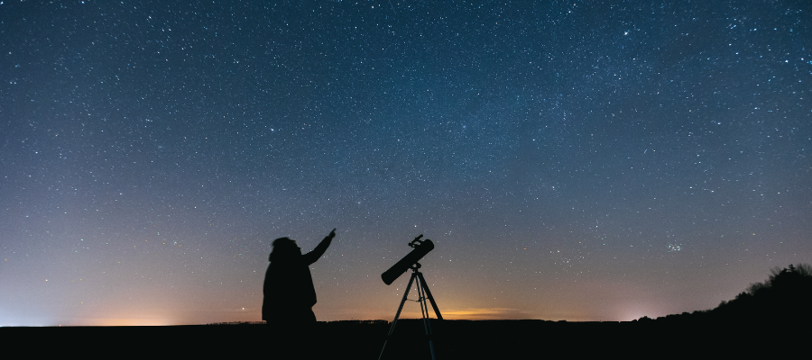 Person stargazing with telescope under dark sky
